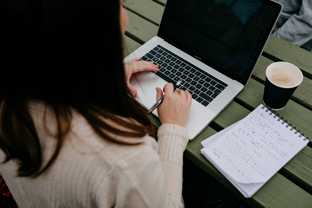 close up of Caroline Stocks on her laptop on a green outdoor table with a coffee